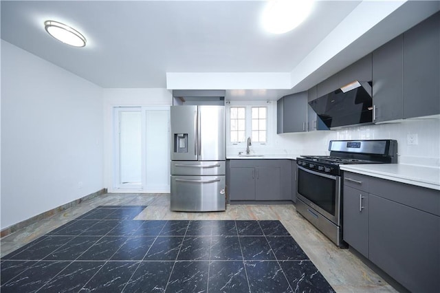 kitchen featuring gray cabinets, a sink, wall chimney range hood, stainless steel appliances, and light countertops