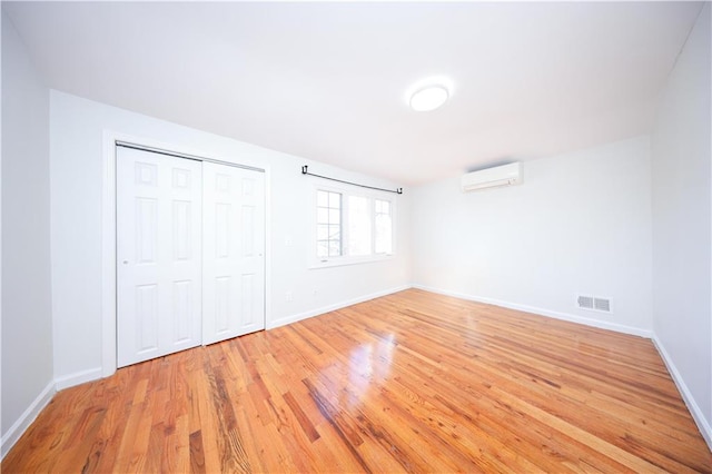 unfurnished bedroom with light wood finished floors, visible vents, a wall mounted AC, and baseboards