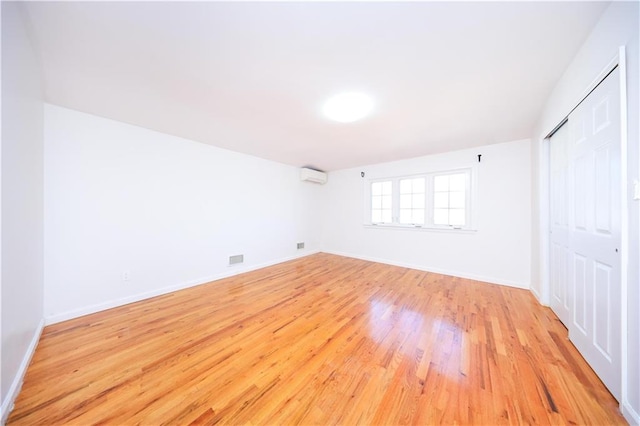 unfurnished bedroom with a closet, baseboards, light wood-style floors, and a wall unit AC