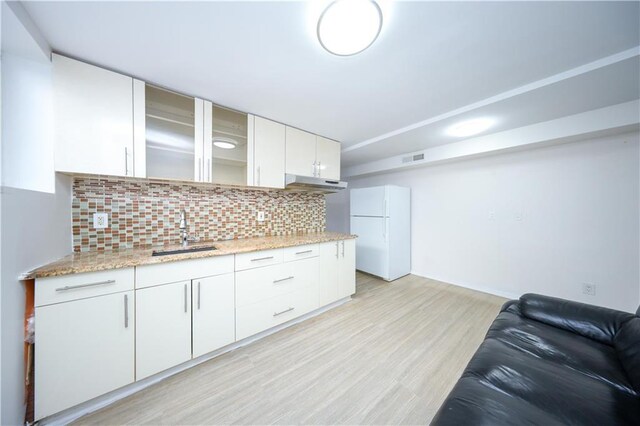 kitchen featuring light wood-style flooring, freestanding refrigerator, a sink, white cabinets, and backsplash