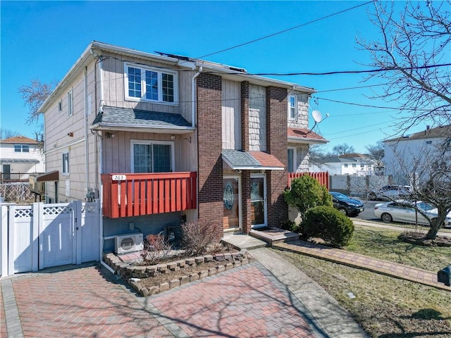 view of front facade featuring brick siding, a shingled roof, fence, ac unit, and a gate