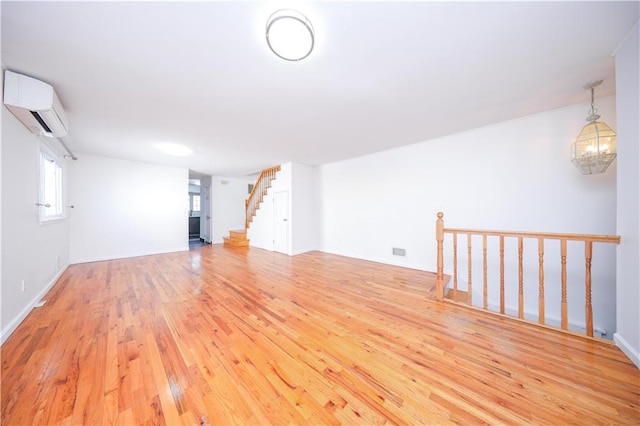 spare room featuring a wall unit AC, wood finished floors, visible vents, an inviting chandelier, and stairs