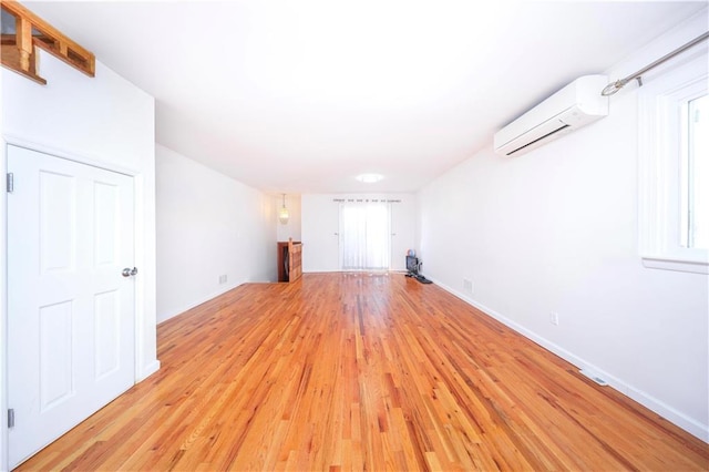 unfurnished living room with a wall unit AC, light wood-style flooring, and baseboards