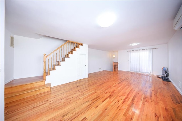 unfurnished living room with stairway, an AC wall unit, visible vents, and wood finished floors