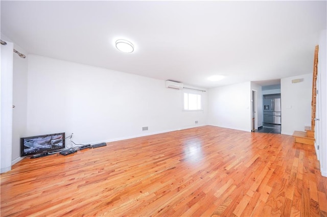 spare room featuring light wood-style flooring, baseboards, and a wall mounted AC