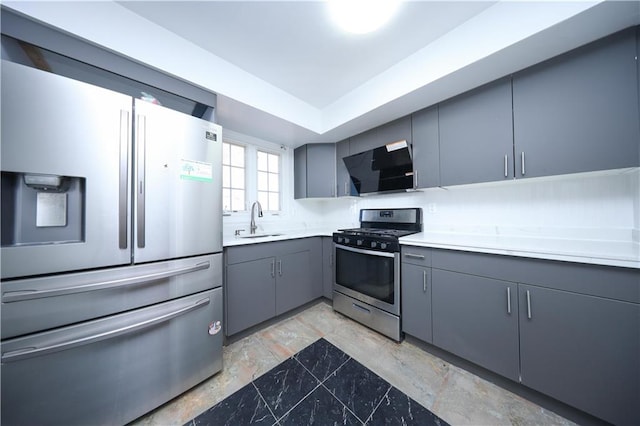 kitchen featuring gray cabinetry, ventilation hood, light countertops, appliances with stainless steel finishes, and a sink