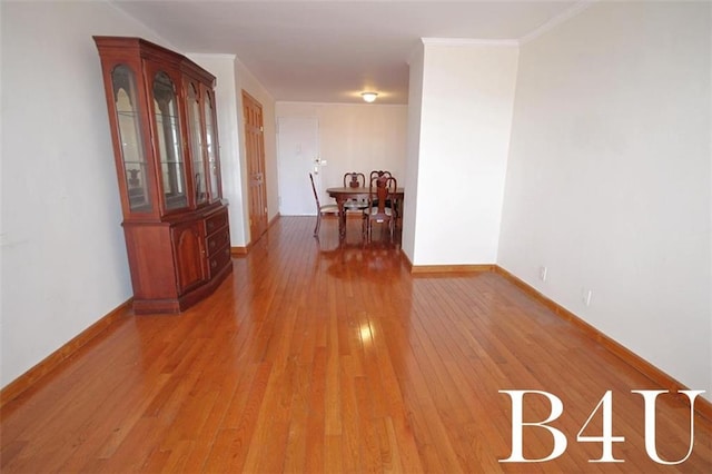 corridor featuring baseboards, ornamental molding, and light wood-style flooring