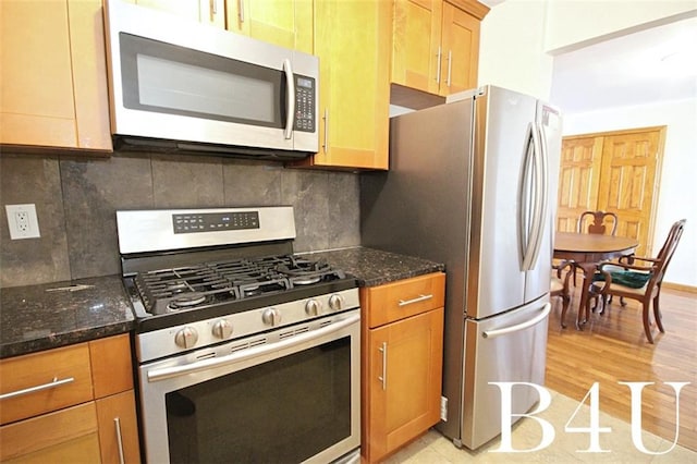 kitchen featuring dark stone countertops, appliances with stainless steel finishes, light wood-style floors, and tasteful backsplash