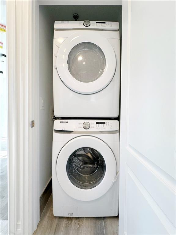 laundry room with laundry area, stacked washer / dryer, and light wood finished floors