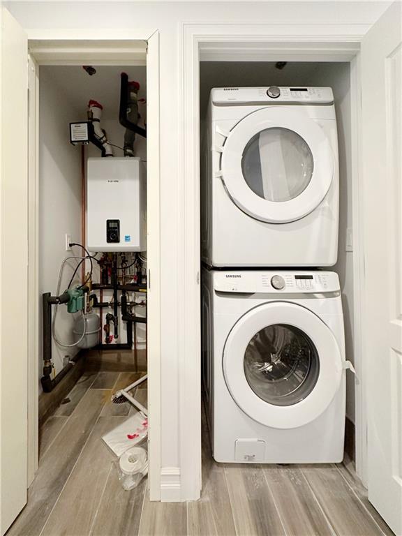 washroom with stacked washer and clothes dryer, wood finished floors, water heater, and laundry area