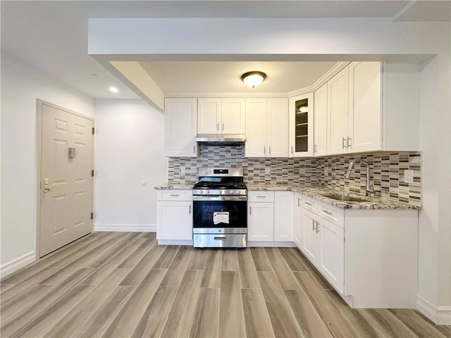 kitchen featuring stainless steel gas stove, a sink, under cabinet range hood, light stone counters, and decorative backsplash