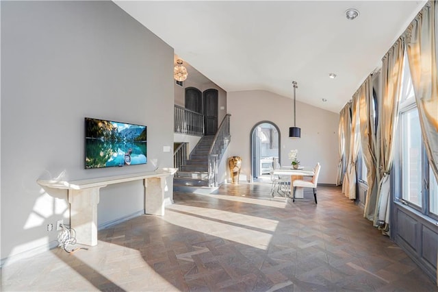 living room featuring arched walkways, high vaulted ceiling, stairs, and baseboards