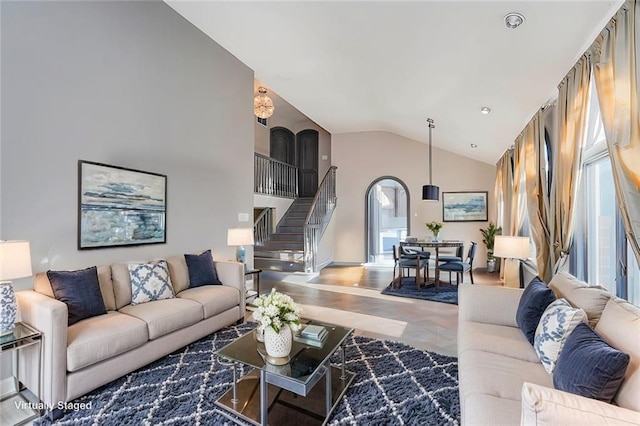 living room featuring arched walkways, stairway, and high vaulted ceiling