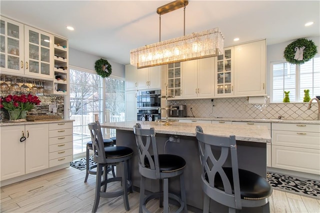 kitchen featuring backsplash, double oven, a breakfast bar area, light wood-style flooring, and white cabinets