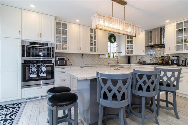 kitchen featuring a kitchen bar, tasteful backsplash, a center island, stainless steel double oven, and wall chimney exhaust hood