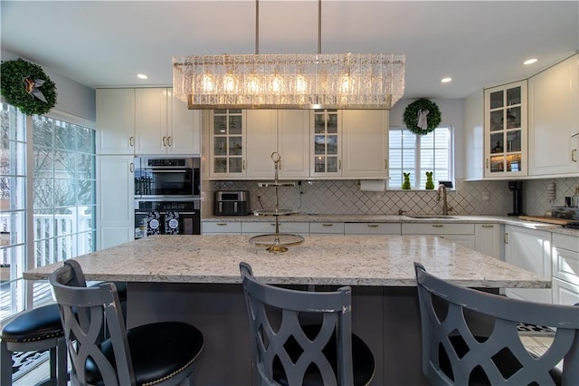 kitchen featuring stainless steel double oven, a breakfast bar, a sink, white cabinets, and tasteful backsplash