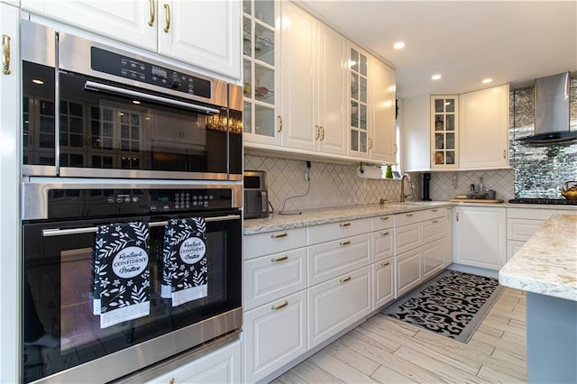 kitchen with gas cooktop, stainless steel double oven, a sink, wall chimney exhaust hood, and tasteful backsplash