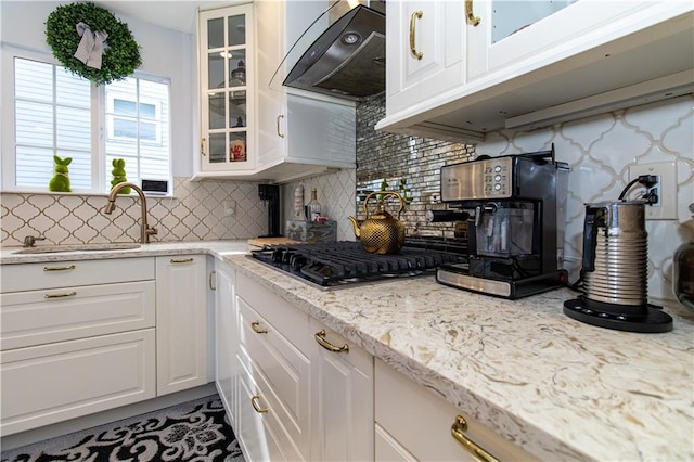 kitchen featuring glass insert cabinets, extractor fan, stainless steel gas stovetop, white cabinetry, and a sink