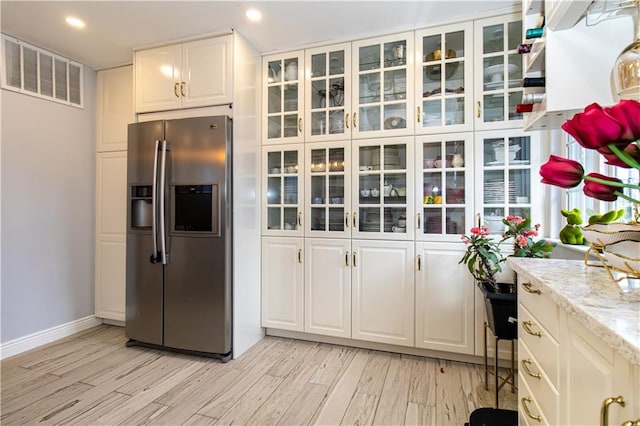 kitchen featuring light wood finished floors, visible vents, glass insert cabinets, stainless steel refrigerator with ice dispenser, and white cabinets