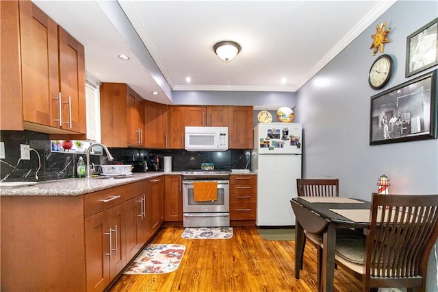 kitchen featuring white appliances, wood finished floors, a sink, crown molding, and brown cabinets