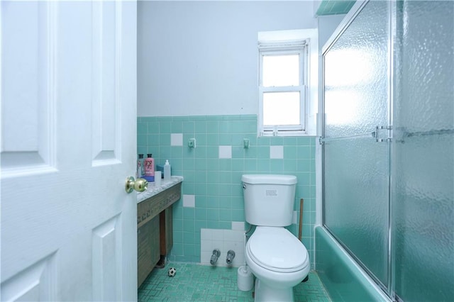 full bathroom with tile patterned floors, toilet, combined bath / shower with glass door, tile walls, and wainscoting