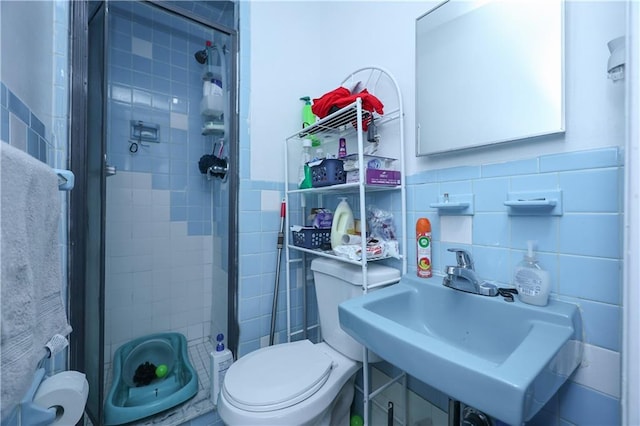 bathroom featuring tile walls, toilet, a stall shower, and a sink