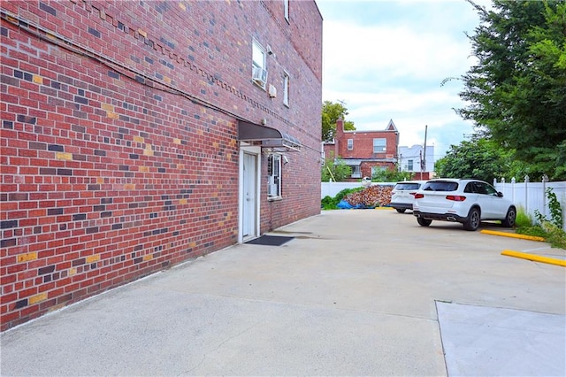 view of property exterior with brick siding, uncovered parking, and fence