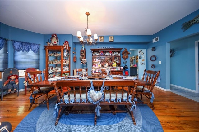 dining space with baseboards, wood finished floors, visible vents, and a chandelier