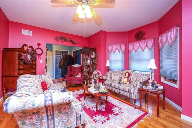 living room featuring ceiling fan, visible vents, baseboards, and wood finished floors