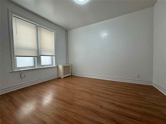 spare room featuring baseboards, wood finished floors, and radiator heating unit