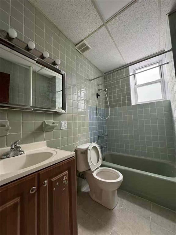 bathroom with tile patterned flooring, backsplash, toilet, shower / bathing tub combination, and tile walls