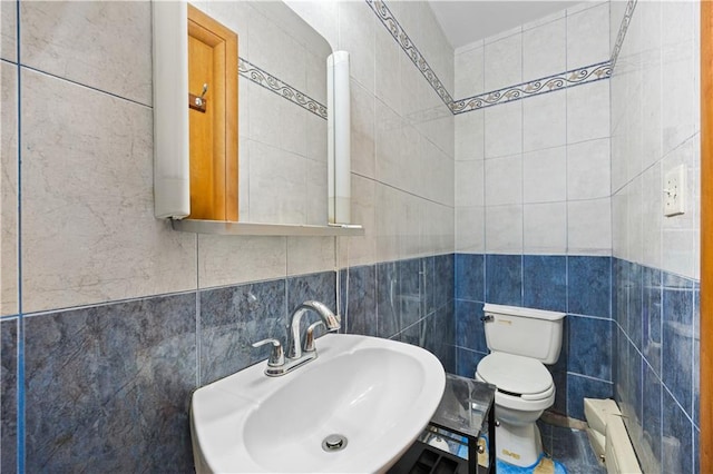 half bath with tile walls, toilet, a baseboard radiator, and a sink