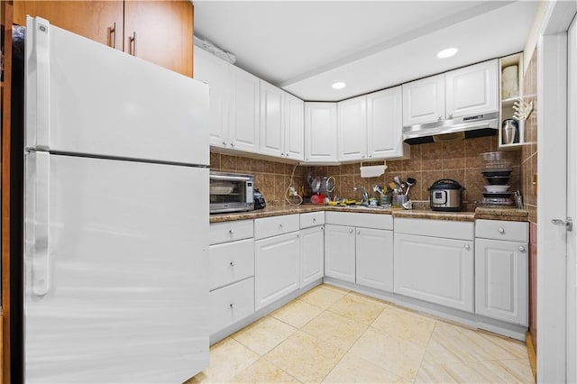 kitchen featuring under cabinet range hood, decorative backsplash, white cabinetry, and freestanding refrigerator