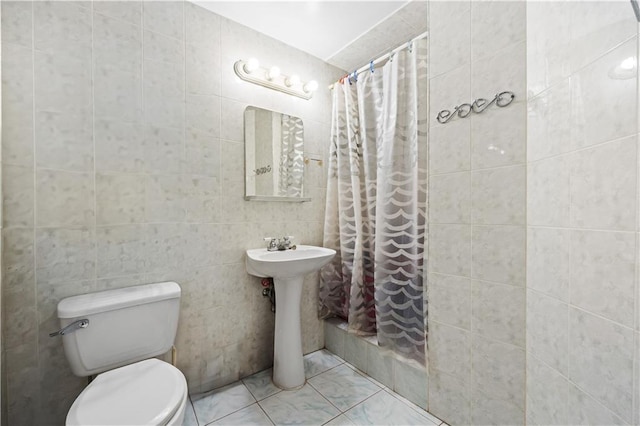 bathroom featuring toilet, tiled shower, tile walls, and a sink