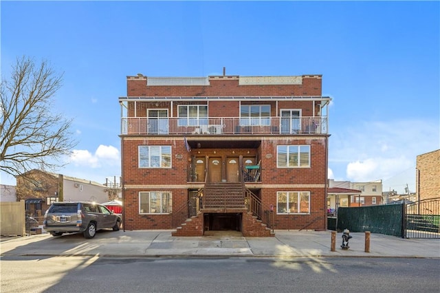 view of front of property featuring a balcony, fence, and brick siding