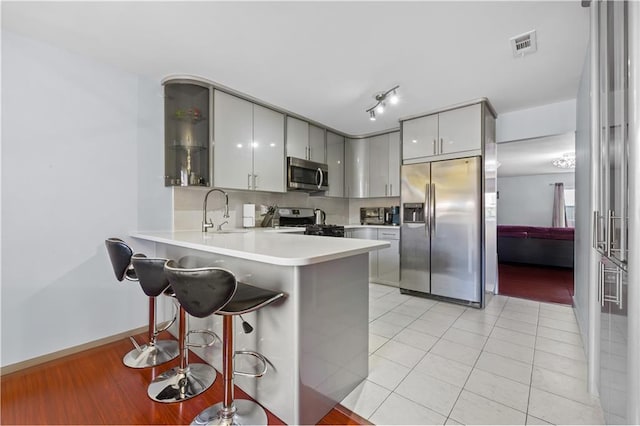 kitchen with visible vents, a sink, a kitchen breakfast bar, appliances with stainless steel finishes, and a peninsula