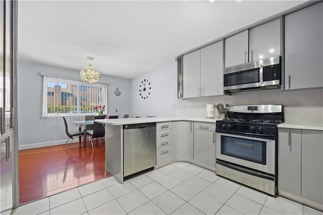 kitchen featuring stainless steel appliances, a peninsula, gray cabinets, and light countertops