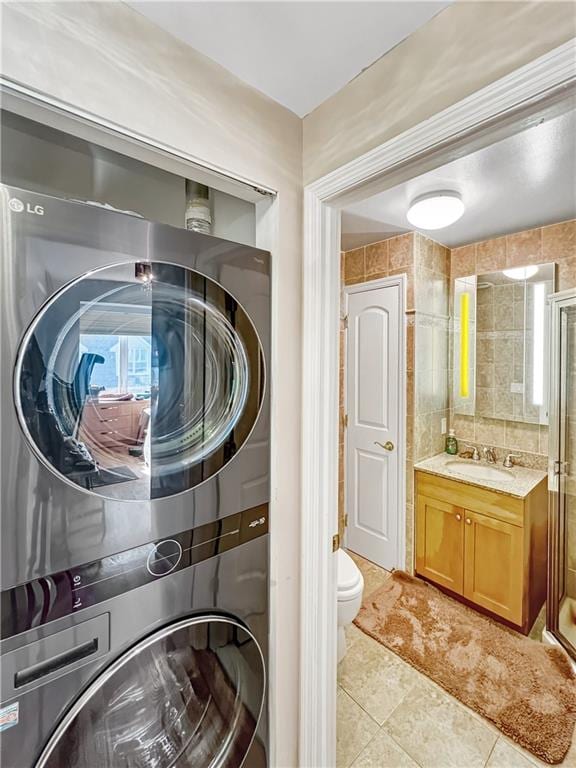 washroom featuring light tile patterned floors, laundry area, a sink, stacked washer and dryer, and tile walls