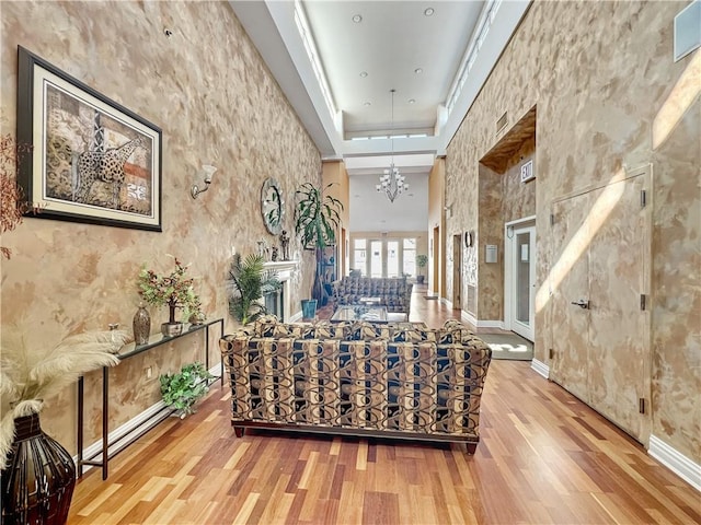 living area featuring a notable chandelier, wood finished floors, baseboards, and a towering ceiling