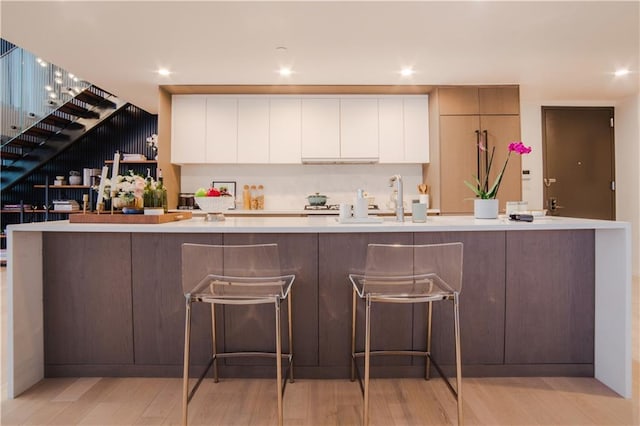 kitchen with light wood finished floors, recessed lighting, a large island with sink, light countertops, and white cabinetry