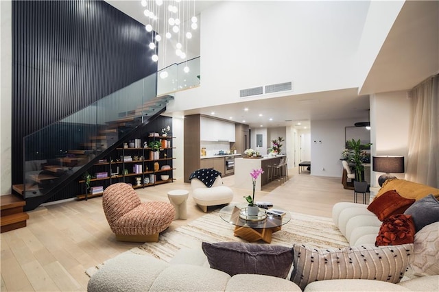 living room featuring visible vents, a high ceiling, stairs, light wood-style floors, and a notable chandelier