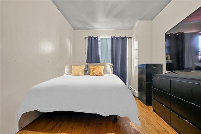 bedroom featuring a baseboard heating unit and light wood-style flooring