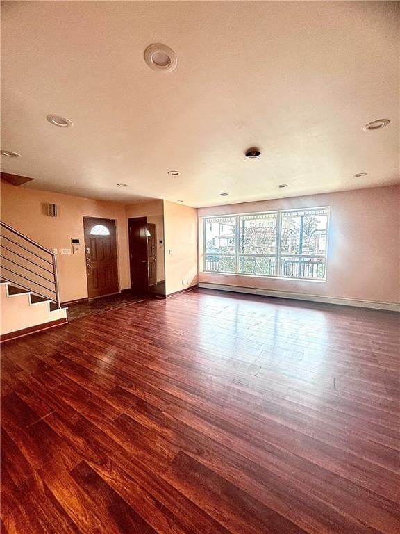 unfurnished living room with stairs, wood finished floors, and baseboards