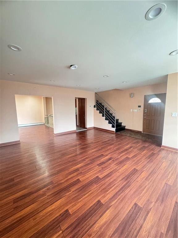 unfurnished living room featuring stairway, baseboards, and wood finished floors