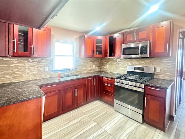 kitchen with dark stone countertops, a sink, decorative backsplash, dark brown cabinets, and appliances with stainless steel finishes