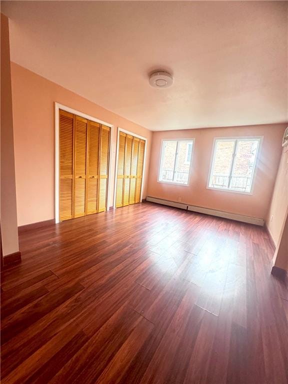 unfurnished room featuring dark wood-style floors, baseboards, and a baseboard radiator