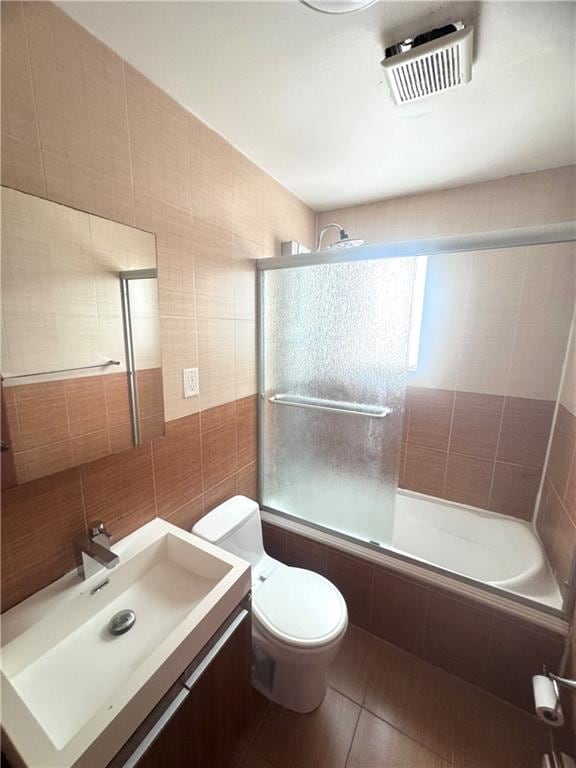 bathroom featuring visible vents, toilet, vanity, tiled shower / bath combo, and tile walls