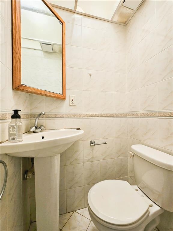 bathroom with tile walls, toilet, and marble finish floor