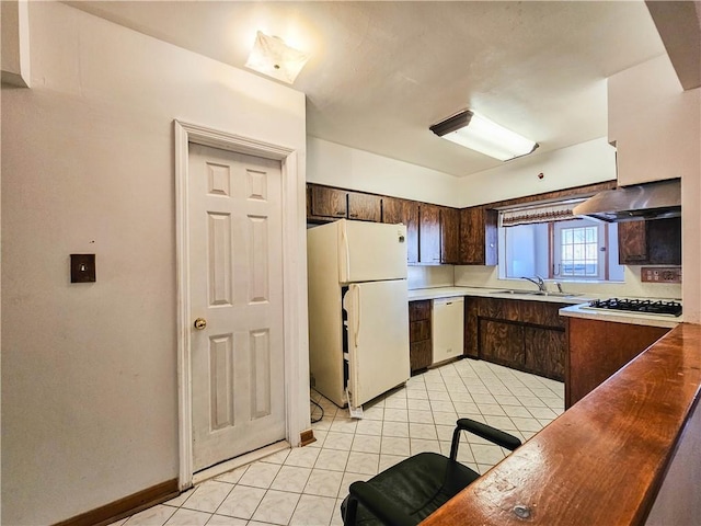 kitchen with a sink, light tile patterned floors, dark brown cabinets, and white appliances