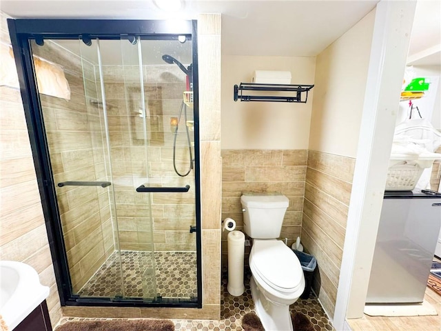 full bath featuring tile walls, toilet, a stall shower, and wainscoting